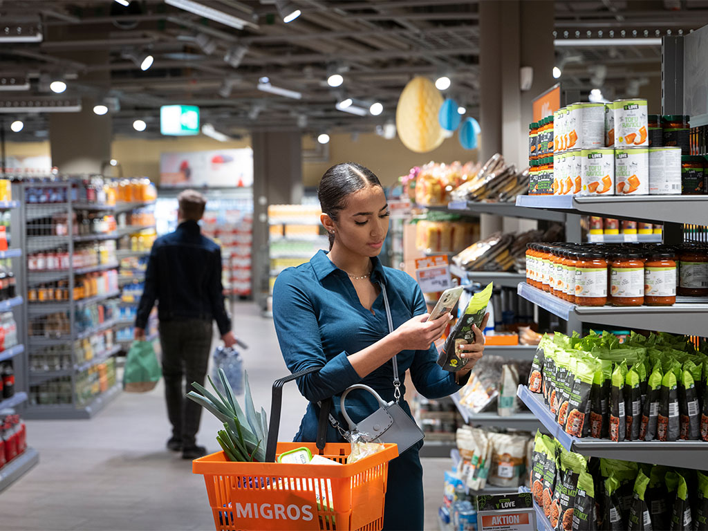 Junge Frau beim Einkaufen im Migros Supermarkt, scannt ihre Ware direkt selbst mit dem eigenen Handy.